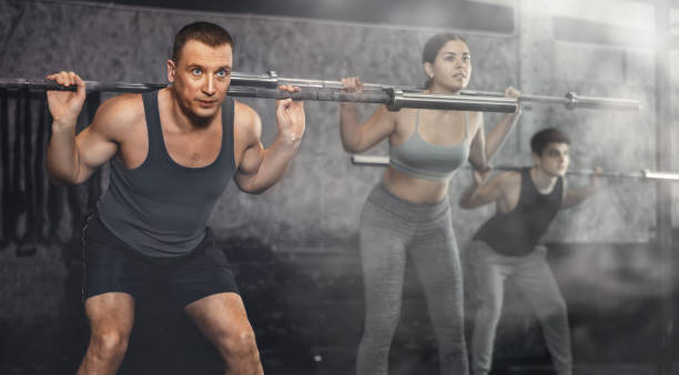 istock Sporty man doing exercises with barbell during group workout 1479510471