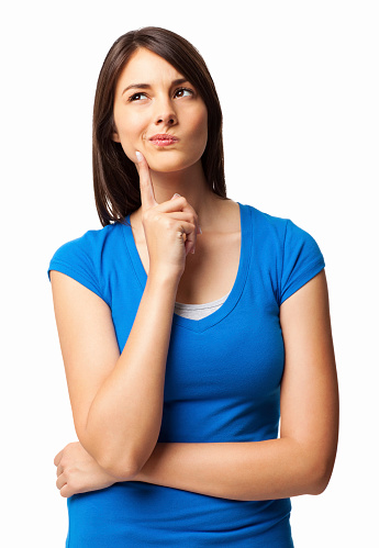 Cute young woman in a casual blue t-shirt thinking with hand on chin. Vertical shot. Isolated on white.