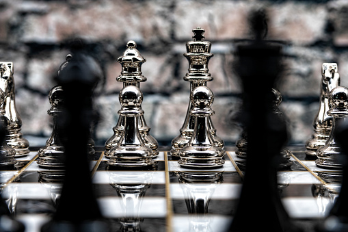 The white king and queen in focus as viewed from between the black king and queen which are out of focus on this chess board before the game begins.