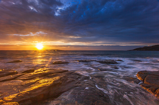 Long exposure seascape of water flowing over rocks with dramatic golden sunset. East Coast, Australia.