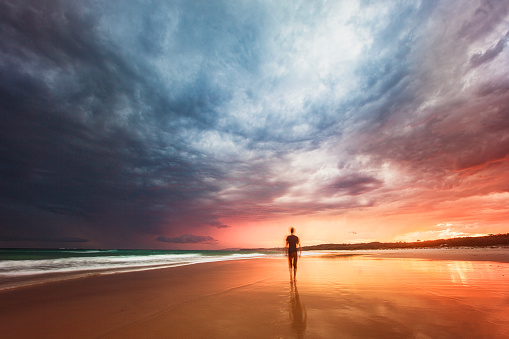 Long exposure seascape of dramatic storm at sunset with young man walking in the golden light. East Coast, Australia.