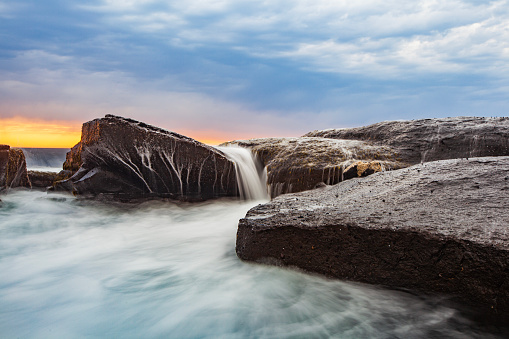 Coastal seascape scene with water rushing over rocks in dramatic light at sunrise