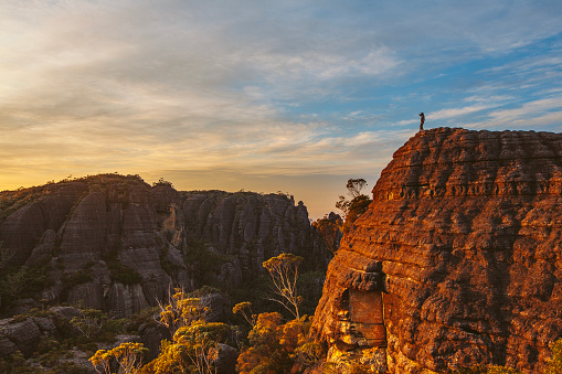 Hiker standing on rock watching sunrise over dramatic mountain landscape. South East Coast, Australia. Budawang Mountain Range.