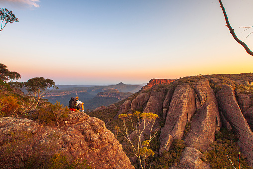 Hiker resting on rock watching sunset over dramatic mountain landscape. South East Coast, Australia. Budawang Mountain Range.