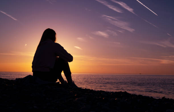 istock A girl is sitting on the beach watching the sunset. 1479518550