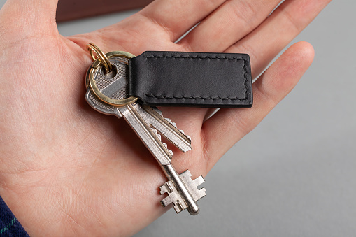 Keys with a black leather keychain in hand on a grey background.  Blank keychain for logo placement. Close up.
