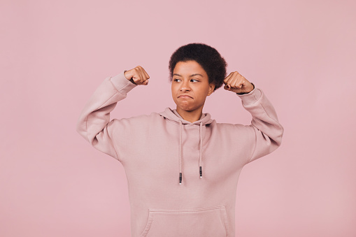 Strong black young woman with raising her hands up against pink background