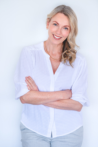 Attractive Mature woman smiling and relaxing and looking at the camera. She is standing against a white wall with her arms crossed