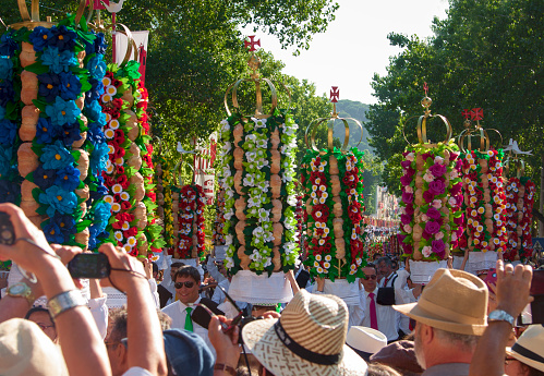 Tomar, Portugal - July 12, 2015: Woman and her chaparone taking part in the tray festival (Festa dos Tabuleiros) in Tomar, Portugal. Dating back hundreds of years, the Festa dos Tabuleiros takes place every four years in Tomar in central Portugal. More than 500 maidens, accompanied by their chaperones, parade for 5 km through the streets carrying baskets of bread decorated with flowers. The basket bears 30 loaves of bread each weighing 400 grams threaded onto 6 canes attached to a wicker basket and topped with a crown and on top is the Cross of Christ or the dove of the Holy Spirit. Hundreds of thousands of visitors are attracted to the event that runs over several days, starting with the elaborate street decoration event.