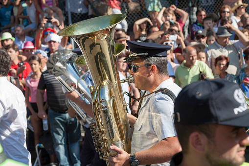 Tomar, Portugal - 12 July 2015. Man playing tuba in a procession with a lot of people in the background.