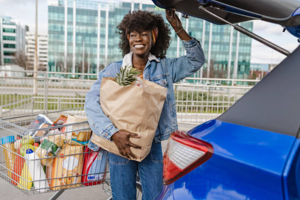Portrait of a happy young African-American woman packing groceries in a car trunk