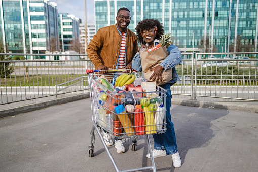 Smiling young African-American couple pulling supermarket cart and looking at the camera