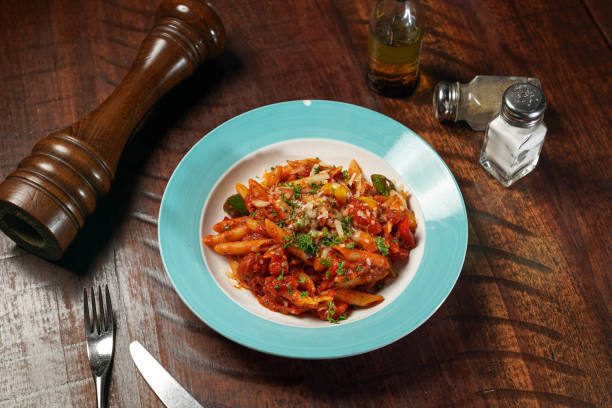 penne arrabbiata mit würziger tomatensauce serviert in einer schüssel isoliert auf einer hölzernen tischplatte blick auf italienisches fast food - penne rigatoni pasta tomato pasta stock-fotos und bilder