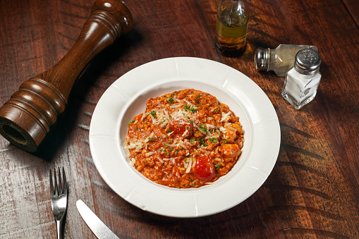 Seafood Risotto with tomato sauce served in dish isolated on wooden table top view of italian fast food