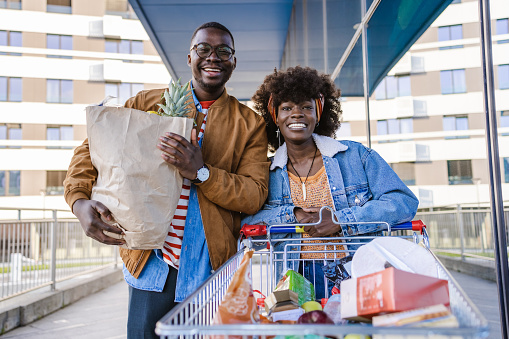 Smiling young African-American couple pulling supermarket cart and looking at the camera