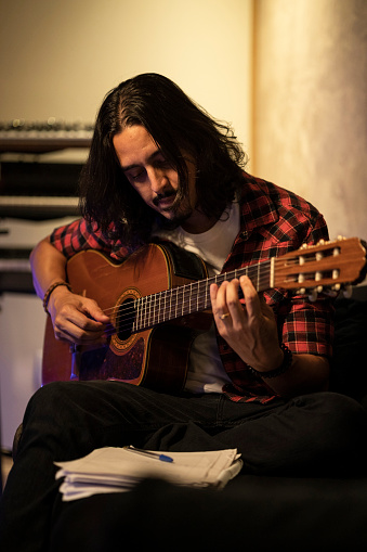 White long haired man with checkered shirt, writing and composing music, singing and playing acoustic guitar at the recording studio