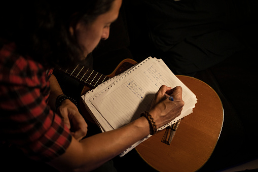 White long haired man with checkered shirt, writing and composing music, singing and playing acoustic guitar at the recording studio