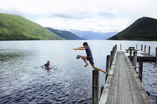 Children jump off a pier on an overcast day in Nelson Lakes, New Zealand.