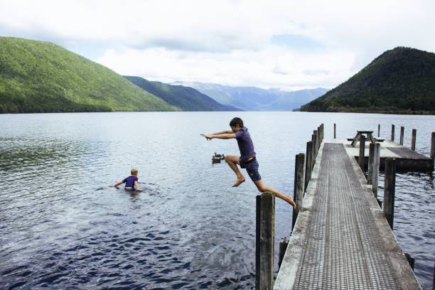 Children Jumping off Pier, Nelson Lakes, New Zealand Children jump off a pier on an overcast day in Nelson Lakes, New Zealand. picton new zealand stock pictures, royalty-free photos & images