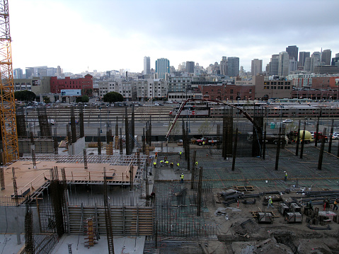 San Francisco - March 25, 2008: People works at High-rise Construction site on ground floor in construction site with a city skyline and Caltrain in the distance.