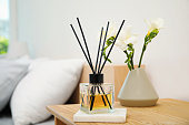 Reed diffuser and vase with bouquet on wooden nightstand in bedroom