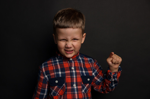 Angry little boy on black background. Aggressive behavior