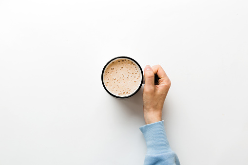 Minimalistic style woman hand holding a cup of coffee on Colored background. Flat lay, top view cappuccino cup. Empty place for text, copy space. Coffee addiction. Top view, flat lay.