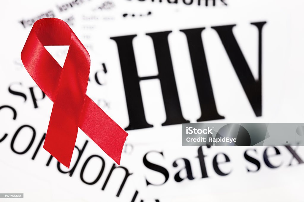 Red AIDS awareness ribbon on HIV related headlines A red AIDS awareness ribbon rests on newspaper headlines relating to HIV and safe sex.  AIDS Stock Photo