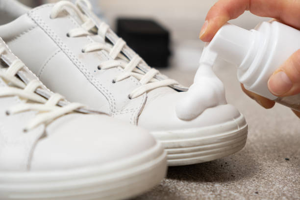 Applying cleaning foam from the bottle to white leather women's sneakers. Care for leather shoes, surface whitening Applying cleaning foam from the bottle to white leather women's sneakers. Care for leather shoes, surface whitening. leather care stock pictures, royalty-free photos & images