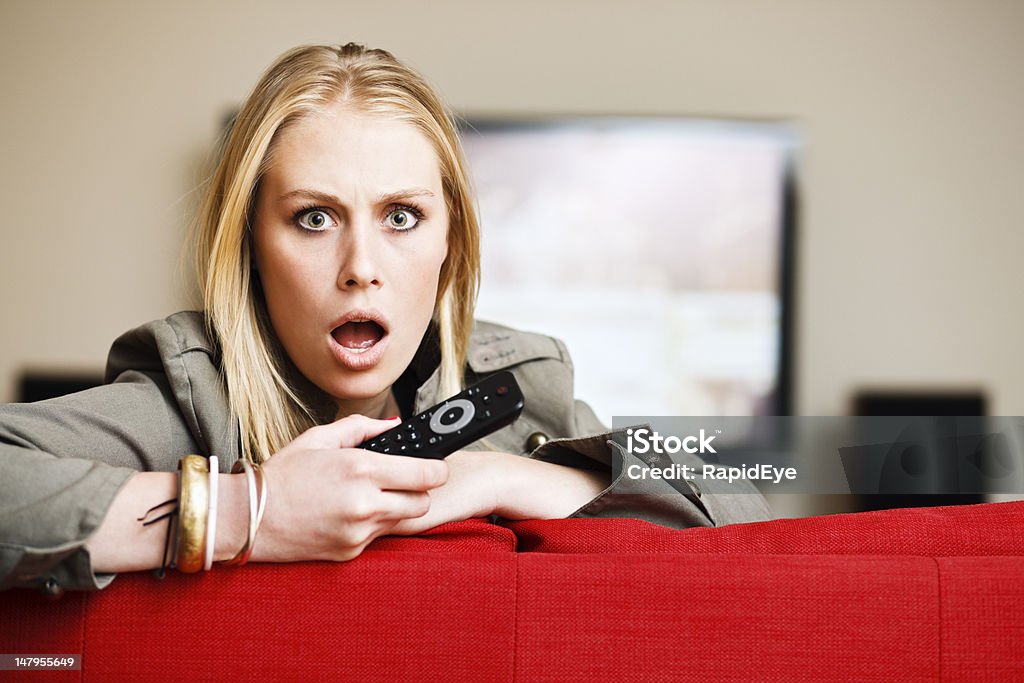 Horrifié blonde babe tenant la télécommande de la télévision est partie - Photo de Télévision libre de droits