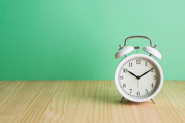 istock White alarm clock, green background on wooden table. 1479559327