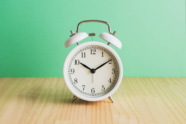 istock White alarm clock, green background on wooden table. 1479559331