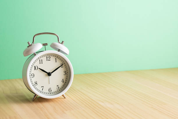 istock White alarm clock, green background on wooden table. 1479559332