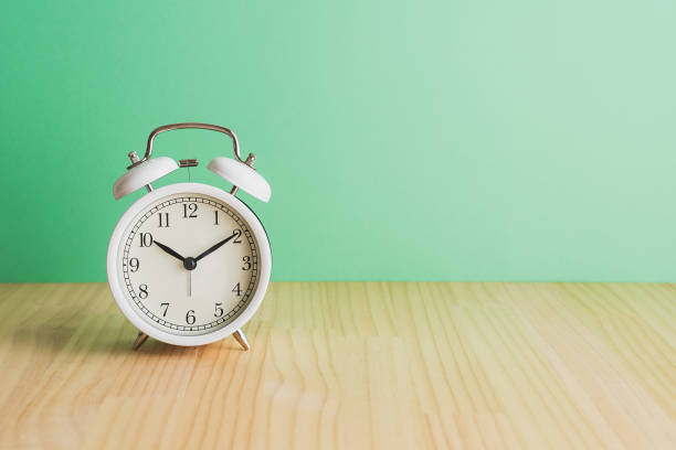 istock White alarm clock, green background on wooden table. 1479559333