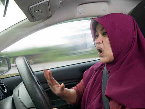 Portrait of Asian muslim female driver mad of trapped in traffic jam,  mischievous reckless way of driving concept with motion blur