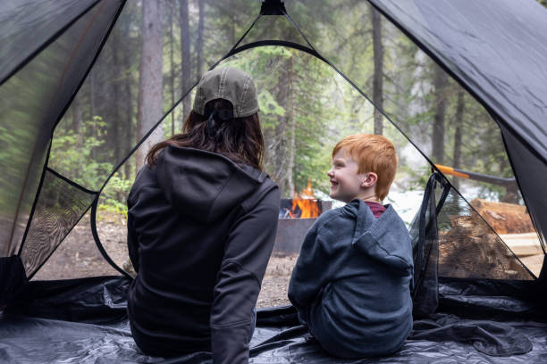 Mãe e filho sentados dentro de uma tenda no acampamento perto da fogueira, Parque Nacional de Yoho, Bc, Canadá - foto de acervo