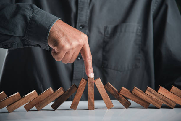 Close up hand stopping or preventing falling block in line with risk project control Close up hand stopping or preventing falling block in line with risk project control, Finger of businessman pointing one wooden to stopping domino effect stopped, Risk protection concept hand stopping dominos stock pictures, royalty-free photos & images