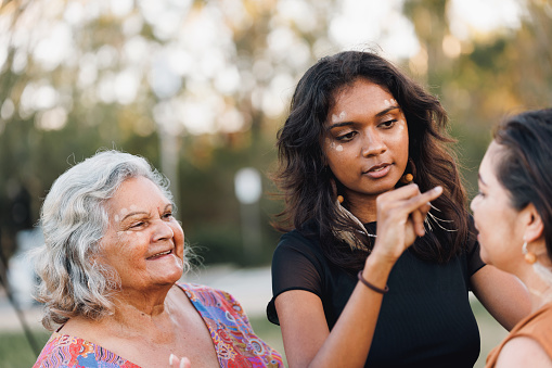 Three Generations Of Aboriginal Australian Women Doing Traditional Ochre Face Painting
