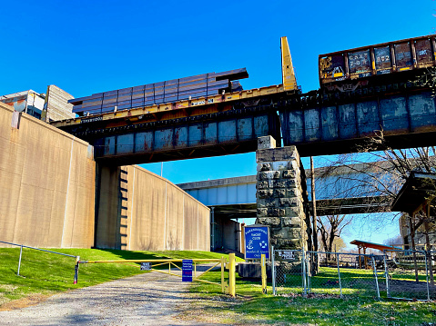 Parkersburg, West Virginia, USA - March 20, 2023: A freight train travels on an elevated train bridge over the closed entrance to the “Parkersburg Yacht Club” entrance.