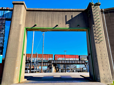 Parkersburg, West Virginia, USA - March 20, 2023: A freight train on an elevated train bridge is framed by a massive, open flood wall gate in downtown Parkersburg on a sunny afternoon.