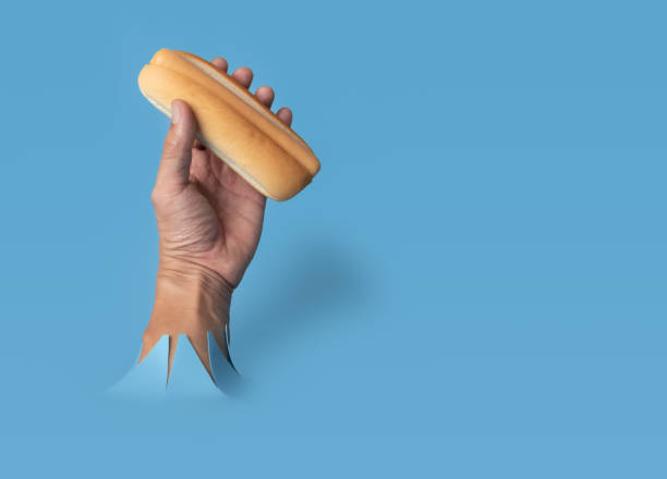 istock Hand hold uncooked hotdog through blue paper background. 1479595339