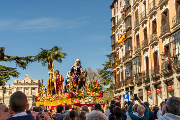 Photo of a religious procession during Semana Santa, the Holy Week, with crowds lining the streets and taking photos during the parade on Palm Sunday. Madrid, Andalusia, Spain - April 2nd 2023. Holy Week in Spain is famous for its religious processions and celebrations. Local residents dress in traditional clothing and participate in the parades that wind through the city streets. They also help with the procession floats, where they are positioned under the float and carry it for the several miles during the Semana Santa procession. selfie madrid photos stock pictures, royalty-free photos & images