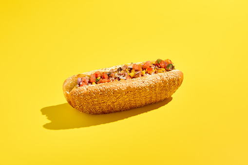 Savor American cheesesteak with marbled beef, vegetable salsa, in a sesame bun on a yellow background. A minimalist, modern approach to food photography highlights this tasty grab-and-go meal.