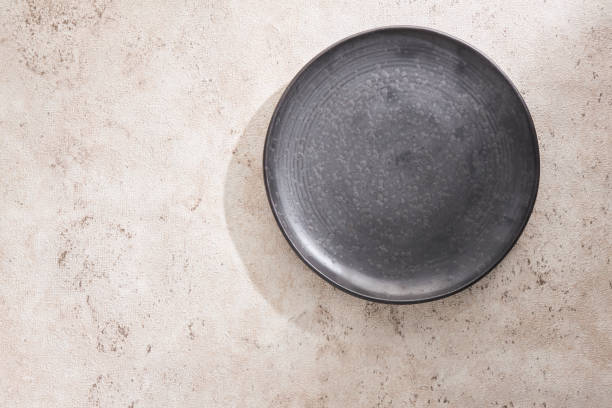 Food menu mockup with dark plate and light background. Empty plate on beige background with shadow. Dark handmade ceramic dish with empty place for restaurant menu concept. Food natural backdrop.