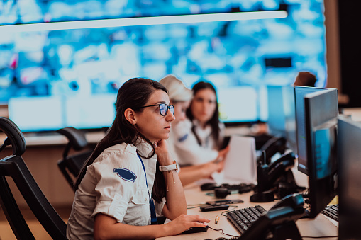 Group of Security data center operators working in a CCTV monitoring room looking on multiple monitors.Officers Monitoring Multiple Screens for Suspicious Activities.