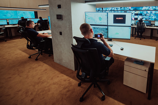 Group of Security data center operators working in a CCTV monitoring room looking on multiple monitors.Officers Monitoring Multiple Screens for Suspicious Activities.