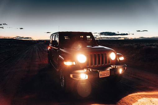 Lone Pine, California, United States - March 8, 2019: Photo of a Jeep Wrangler Sahara 2019 edition parked on a dirt road at dusk close to the city of Lone Pine. It is the new wild offroad vehicle by Jeep. Headlights are on since the pic has been taken after the sunset.