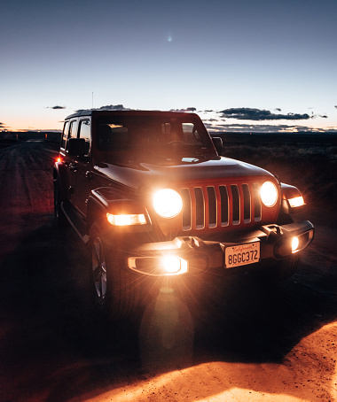 Lone Pine, California, United States - March 8, 2019: Photo of a Jeep Wrangler Sahara 2019 edition parked on a dirt road at dusk close to the city of Lone Pine. It is the new wild offroad vehicle by Jeep. Headlights are on since the pic has been taken after the sunset.