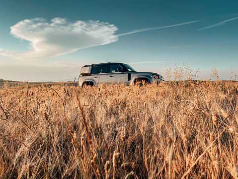 Castelluccio di Norcia, Italy - June 17th, 2021 : The New Land Rover Defender stationery on a gold field of wheat in Tuscany at dusk.