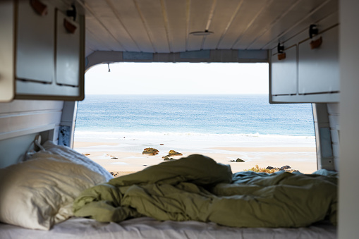 (Selective focus) View of the ocean from inside a van with a dismayed bed in the foreground. Life on the road concept, nomadic lifestyle. Fuerteventura, Canary Islands.